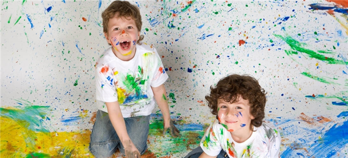 Два молодых парня с брызгами краски на стене, полу, а также на их одежде и коже.