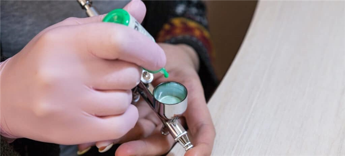 Художник по ногтям добавляет зеленую краску в чашку аэрографа.