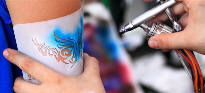 Художник использует трафарет для нанесения рисунка бабочки на ногу человека.