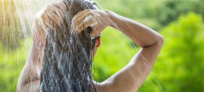 Женщина смывает шампунь с волос в душе на открытом воздухе.