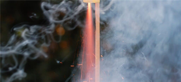 Искры и дым вылетают из нижней части модели ракеты, которая вот-вот взлетит.