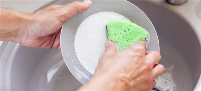 Мужчина моет посуду зеленой губкой.