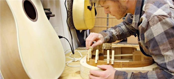 Лютье сгибает кусок дерева внутри рамы при изготовлении гитары ручной работы.