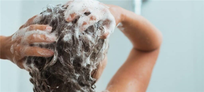 Женщина вспенивает шампунь на волосах во время принятия душа.