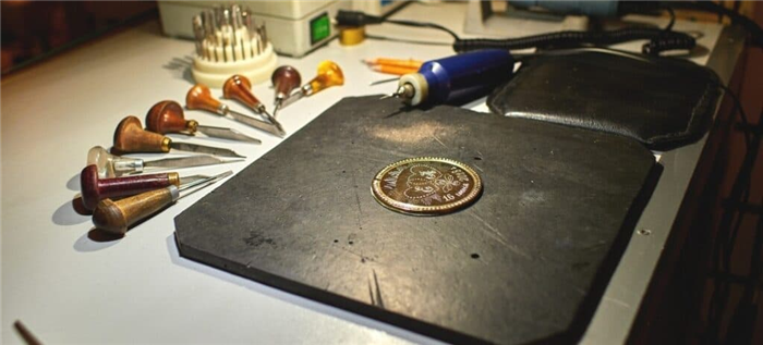 Недавно выгравированный металлический медальон в окружении резцов, выколоток и вращающегося инструмента.