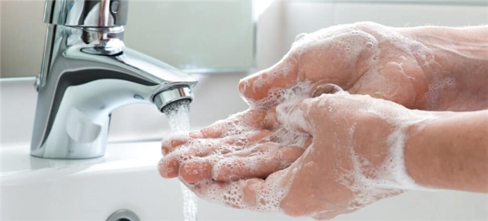 Женщина моет намыленные руки под краном.