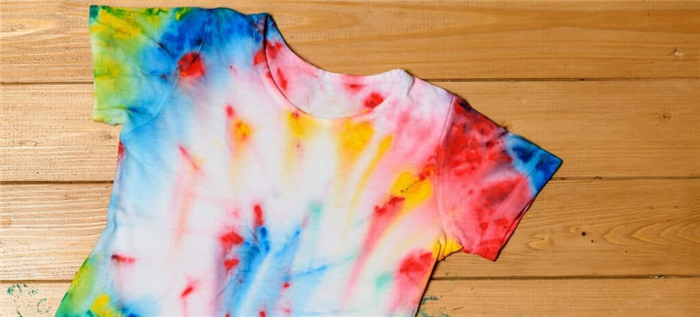 Свежевыкрашенная рубашка с рисунком tie-dye лежит на деревянном столе с несколькими пятнами вокруг рубашки.