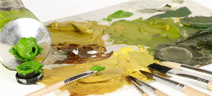 Открытый тюбик зеленой масляной краски лежит на недавно использованной палитре с несколькими кистями.