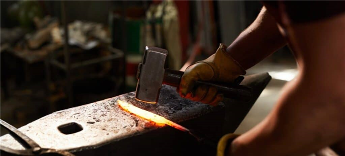 Кузнец использует молот и наковальню для придания формы куску раскаленного металла.