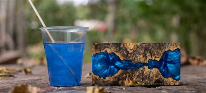 Чашка со смолой голубого оттенка стоит рядом с маленькой картиной из смолы на улице.