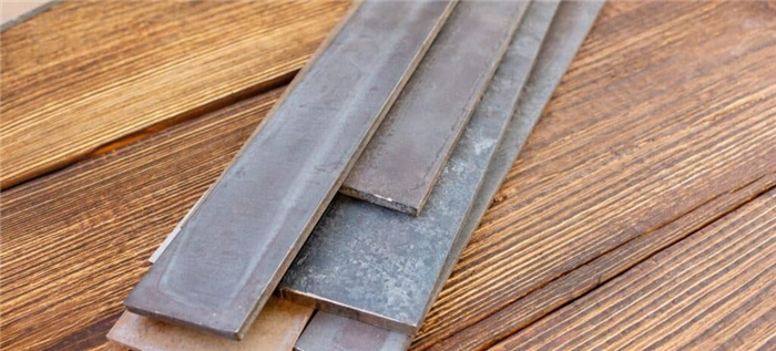 Ассортимент стальных заготовок для изготовления ножей на деревянном столе.