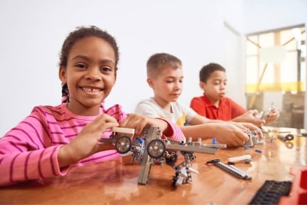 Три юных студента играют с роботизированными игрушками STEM.