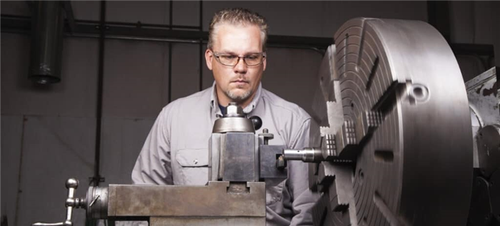 Мужчина использует токарный станок по металлу для обработки куска металла.