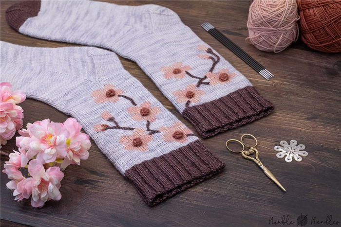 детальный снимок носков с цветущей сакурой и различными инструментами для вязания на заднем плане