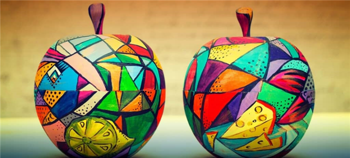 Пара деревянных яблок, окрашенных различными современными рисунками в яркие цвета.