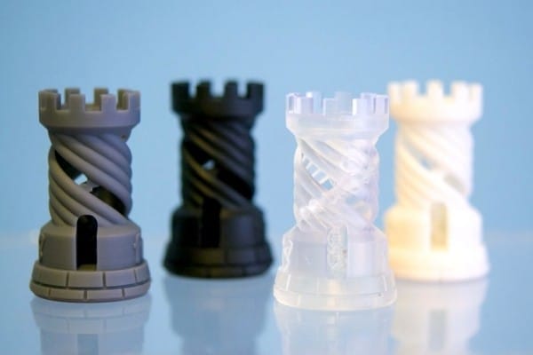 Серые, черные, прозрачные и белые 3D-печатные шахматные фигуры из смолы на светло-голубом фоне.