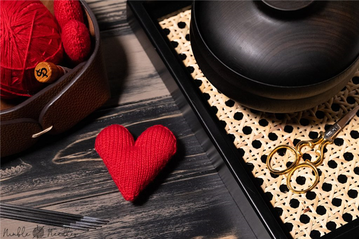 узор для вязания идеального красного сердца на черном подносе с материалами для вязания на заднем плане