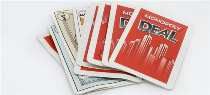 Колода карт Monopoly Deal, разложенная на белом фоне.