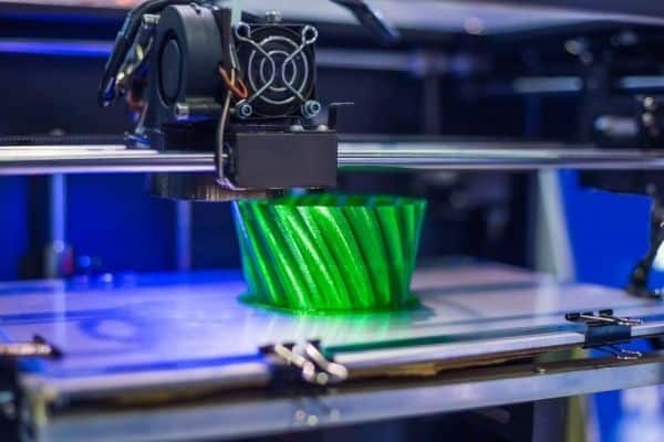 3D-принтер печатает ярко-зеленую чашку с закрученным дизайном.