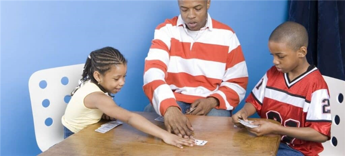 Молодой отец играет в карты с маленькими мальчиком и девочкой.