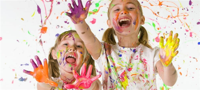 Две молодые девушки с пальчиковыми красками на руках, лицах и одежде.