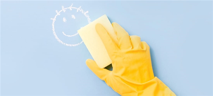 Рука в желтой перчатке стирает смайлик со светло-голубой стены.