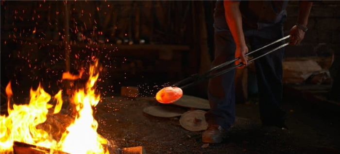 Кузнец снимает раскаленный предмет с огня.