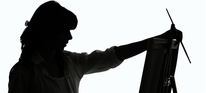 Черно-белое изображение женщины, которая держит кисть с красками, размышляя над своим мольбертом.